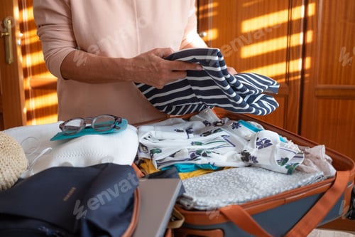 Preview: Senior lady packing her stuff into a suitcase preparing for summer vacation trip