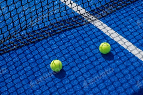 Preview: two paddle tennis balls in the shade of the net of a blue paddle tennis court