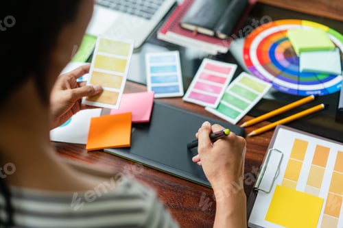 Preview: Creative graphic designer holding color swatch to choosing color and working to designing on tablet