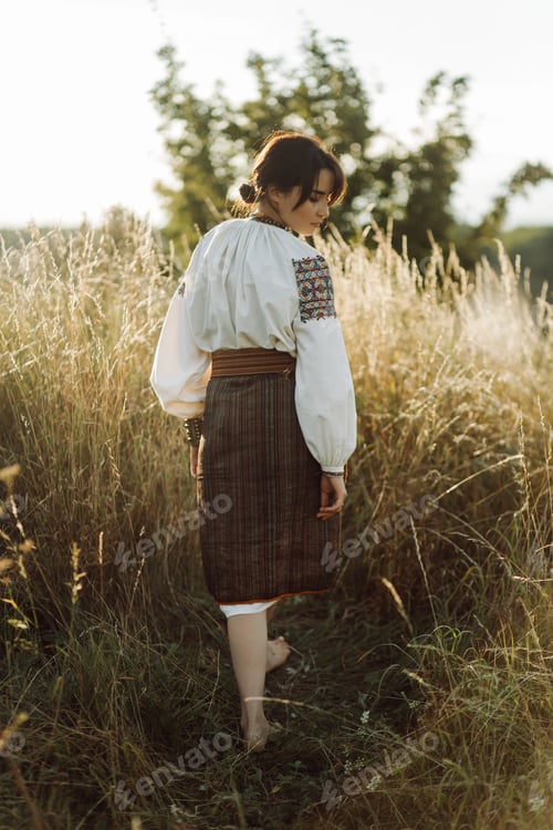 Preview: Young woman in traditional national embroidered shirt and skirt on nature at sunset.
