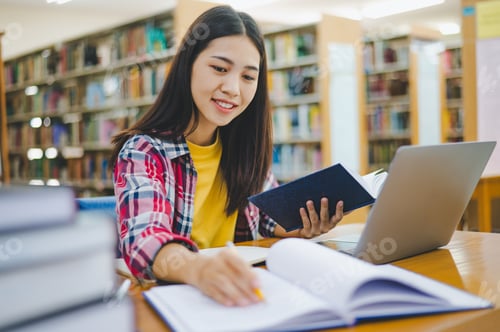 Preview: Female college student working on laptop and searching for books to study
