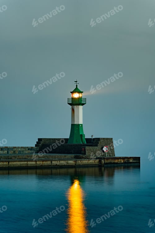 Preview: Vertical of a lighthouse on an illuminated pier reflecting in the sea on Rugen island, Germany