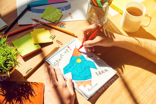 Preview: Just inspired. Close-up top view of man sketching on paper laying on the wooden desk