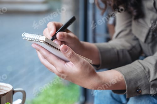 Preview: Closeup image of a woman's hands holding and writing on blank notebook
