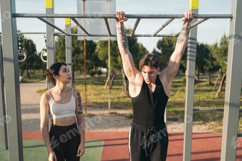 Preview: Young couple preparing pull-ups at outdoor fitness park.