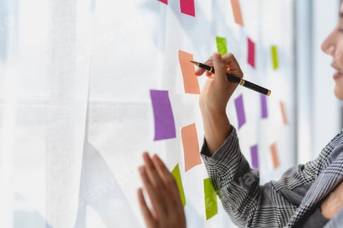 Preview: Asian business woman writing something on sticky notes while working on a business plan at office.