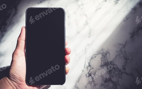 Preview: Hand holding blank screen black mobile phone with sun light shine through window