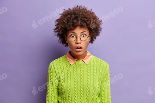 Preview: Portrait of amazed speechless woman with curly hair stares shocked impressed keeps mouth wide opened
