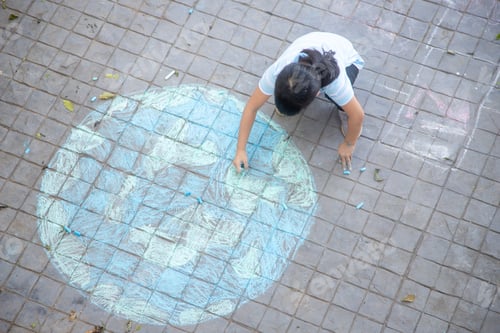 Preview: Asian children play outdoors. Child girl draws a planet globe with a map of the world colored chalk
