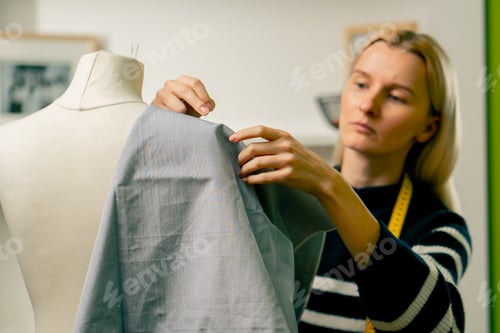 Preview: in sewing workshop seamstress works with a mannequin and pins blue fabric with a pin