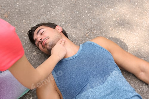 Preview: Young woman checking pulse of unconscious man on street