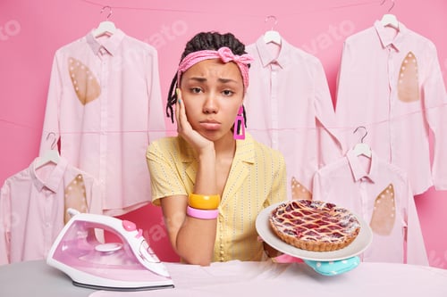 Preview: Sad housewife with braids looks tired and displeased busy doing housework holds delicious cherry pie