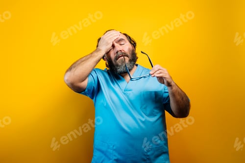 Preview: Bearded man wearing scrubs looking tired