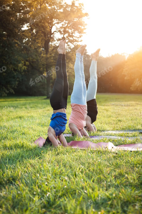 Preview: Yoga at park, group of mixed age women doing salamba sirsasana pose headstand exercise