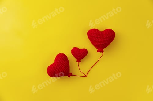 Preview: three knitted red heart-shaped balloons in row on yellow background, concept of love and family