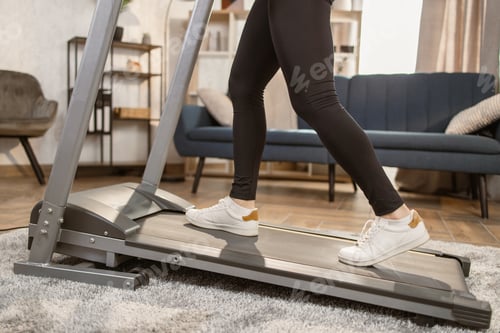 Preview: Close-up of female feet sneakers woman treadmill running in a modern apartment
