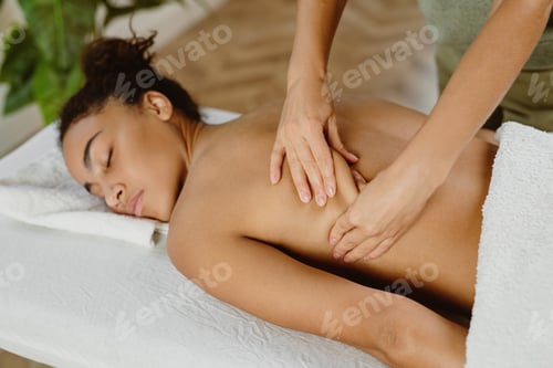 Preview: African American woman getting relaxing back massage in spa salon.