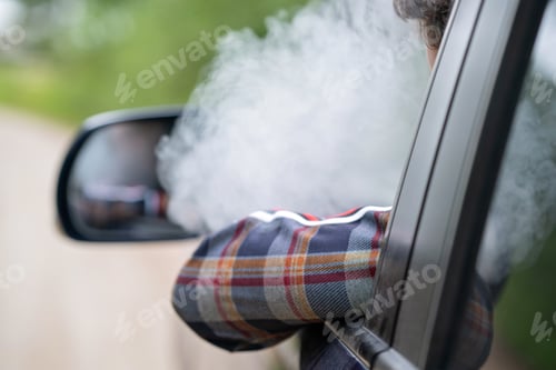 Preview: a young man sits behind the wheel in a car and smokes an electronic cigarette