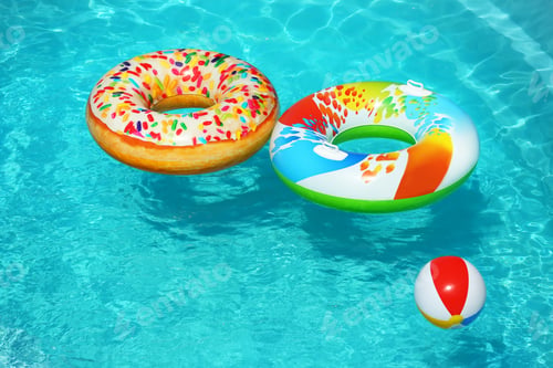 Preview: Bright inflatable rings and beach ball floating in swimming pool on sunny day. Space for text