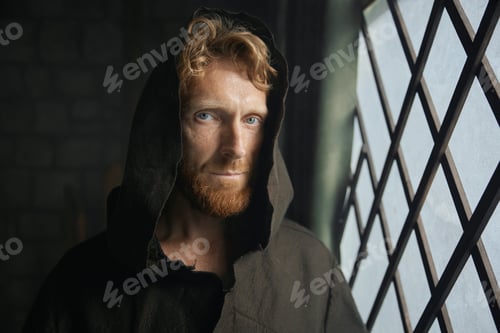Preview: Portrait of pensive monk in medieval costume with hood looking through window of monastery