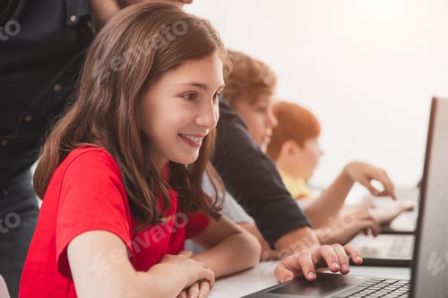 Preview: Happy schoolgirl with teacher using laptop during lesson