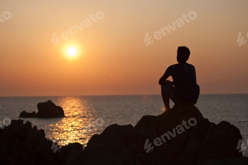 Preview: Silhouette of man on rocks looking away at sunset over sea, Olbia, Sardinia, Italy
