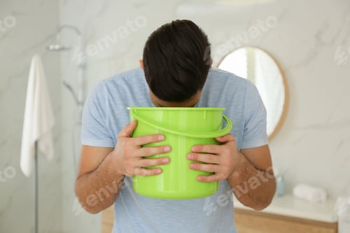 Preview: Man with bucket suffering from nausea in bathroom. Food poisoning