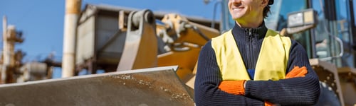 Preview: Cheerful male engineer standing near tractor at factory