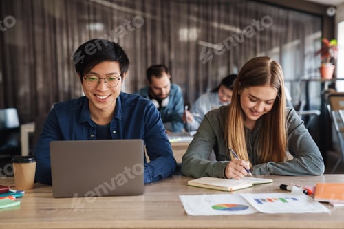 Preview: Photo of joyful students using laptop and writing in exercise book