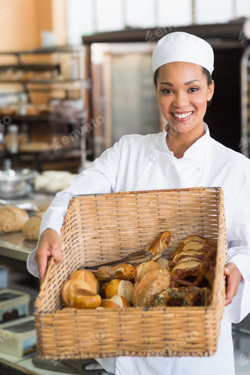 Preview: African American baker standing in bakery holding wicker basket of breads and pastries, smiling