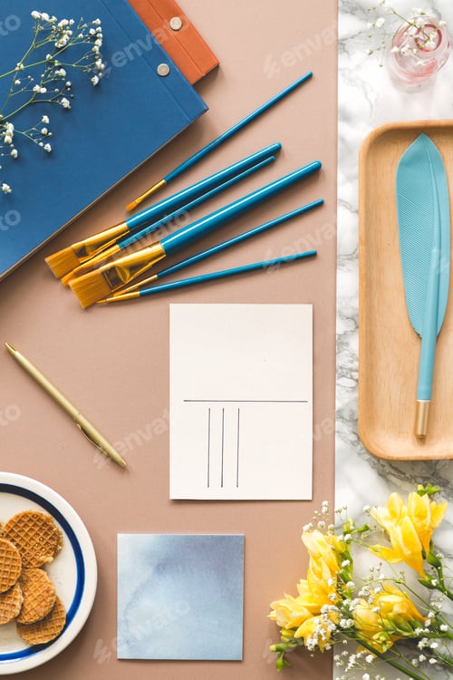 Preview: Top view on paint brushes and postcard on desk with yellow flowe