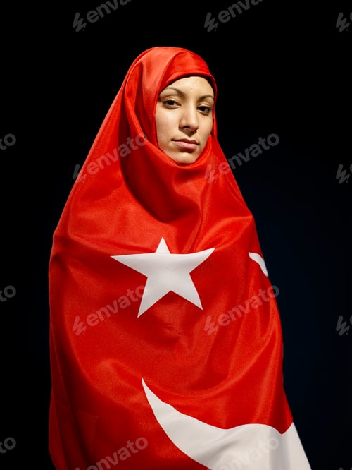 Preview: A person draped in a Turkish flag with a white star and crescent looking into the camera