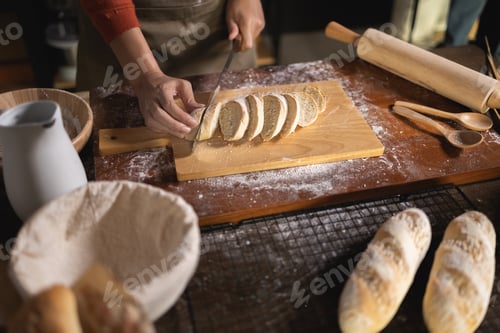 Preview: Top view of baker Using knife to cut Baguette on kitchen table