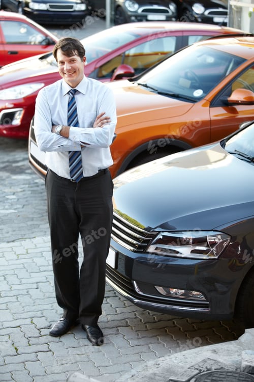 Preview: A man standing confidently and smiling in the lot of his dealership