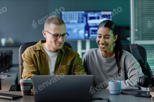 Preview: Two Smiling Programmers Cooperating Using Laptop at Desk during Work Meeting in Office