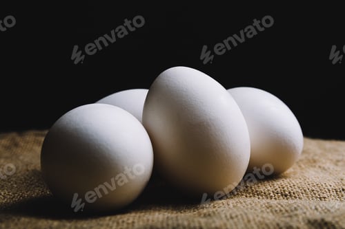 Preview: Closeup shot of four white eggs on a brown surface on a black background
