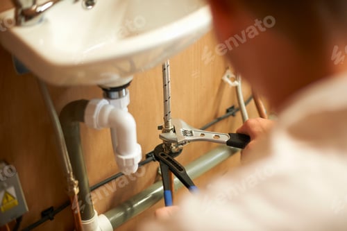 Preview: Male trainee plumber using adjustable spanner on pipework in college workshop