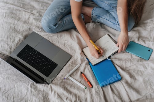 Preview: Cropped shoot of girl writing in diary sitting on bed with laptop phone pen, remote learning home.