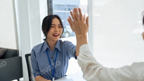 Preview: happy Asian female office worker gives high fives to a male colleague, celebrating project success