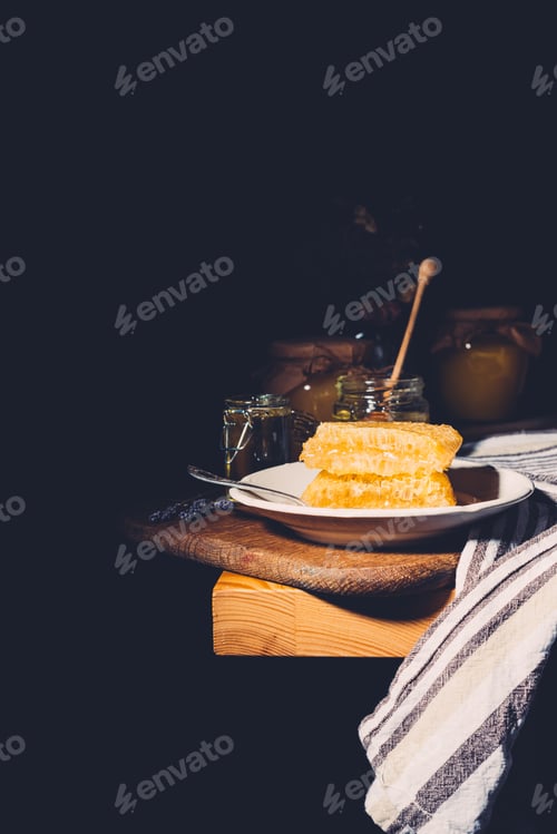 Preview: selective focus of plate with honeycombs and jars with honey on black background