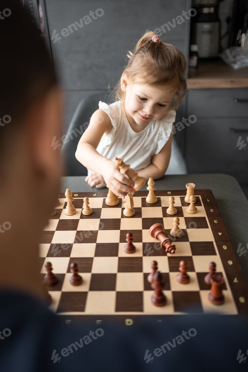 Preview: Father teaching his little daughter to play chess at the table in home kitchen. The concept early
