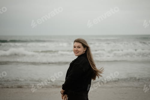 Preview: young girl smiling while standing on the beach, hair fluttering