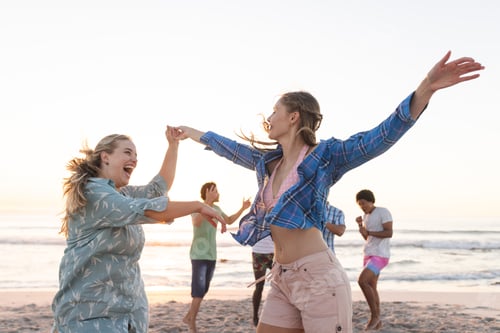 Preview: Young women dance on the beach at sunset, with copy space