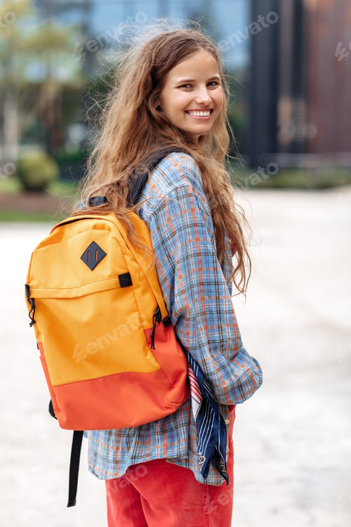 Preview: Attractive young blonde hipster woman student with backpack looking back to camera with happy face.