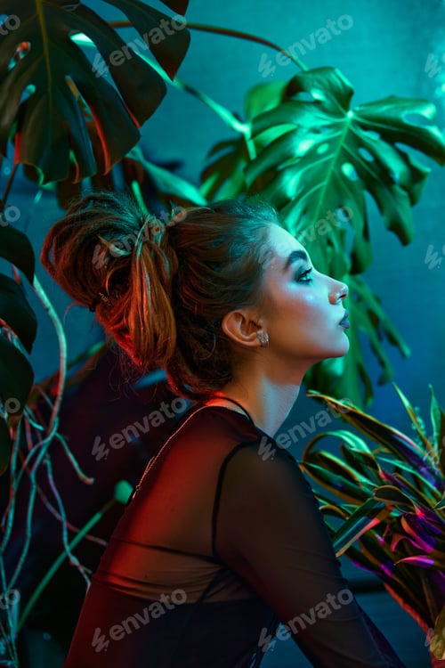 Preview: Young woman surrounded by vibrant tropical plants, wearing black leather outfit and long-sleeved