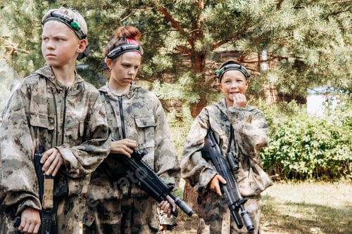 Preview: Group of teenage boys and girl with weapon in hands in camouflage playing laser tag shooting game
