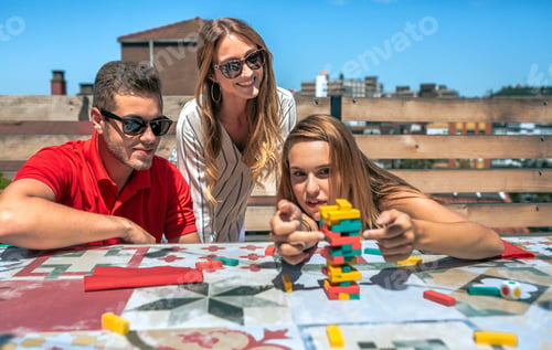 Preview: Concentrated woman pushing game piece next to her friends in a rooftop party