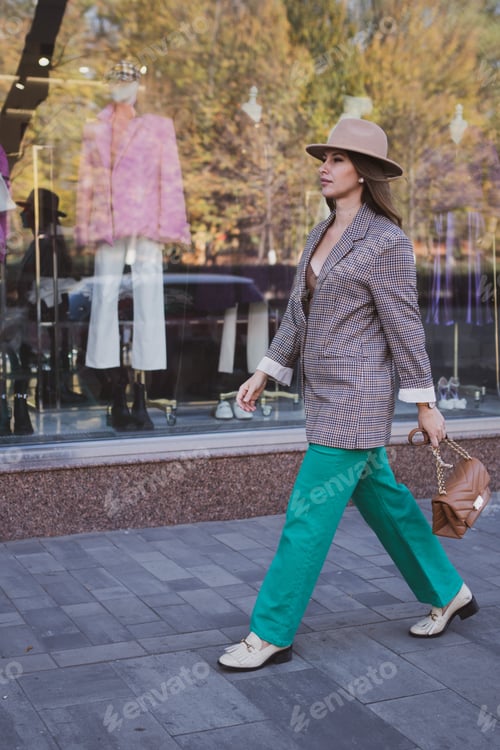 Preview: Stylish business woman in jacket and felt hat walks on the city street