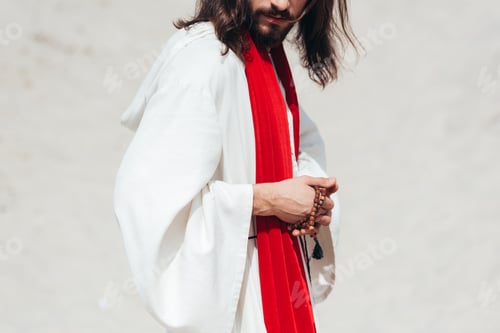 Preview: cropped image Jesus in robe and red sash holding rosary in desert