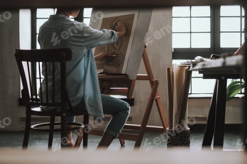 Preview: Rare View Of The Young Talented Artist Sitting In Front Of The Easel In Art Studio And Shading The